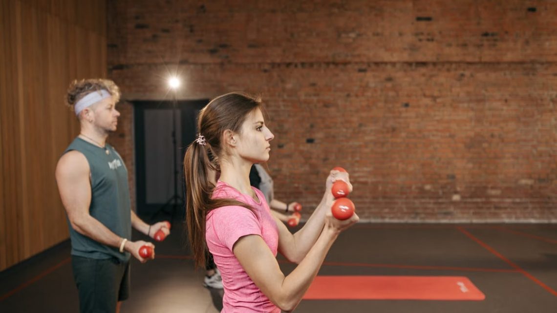 Group of adults exercising indoors with dumbbells, focused on fitness and health.